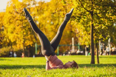 Sonbaharda parkta pilates yapan yetişkin bir kadın. Sağlıklı bir yaşam tarzı. Makas egzersizi..