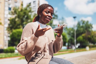 Genç siyah kadın akıllı telefon kullanıyor. Sesli mesaj kaydediyor..