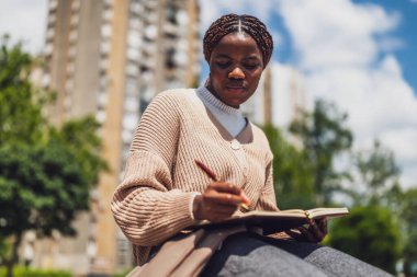 Neşeli Afrikalı Amerikalı kadın şehir parkında dinleniyor, günlüğünü yazıyor..