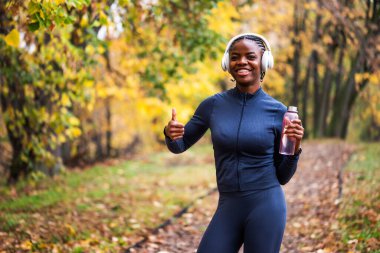 Koşan bir koşucu, rahat ve mutlu görünüyor, canlı sarı ve yeşil yaprakları etrafında canlı bir sonbahar atmosferi yaratıyor..