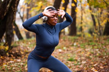 Genç siyah kadın sonbaharda parkta Tai Chi egzersizi yapıyor. Kablosuz kulaklık takıyor..