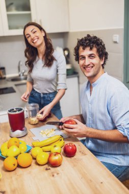 Gülümseyen ve rahatlayan ikili, portakal, elma ve muz dolu bir tezgahla ev yapımı meyve içecekleri hazırlarken birlikte bir an paylaşıyorlar..
