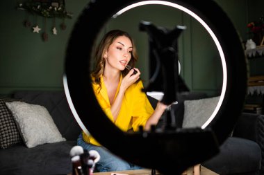 Güzellik vlogcusu evde makyaj dersi çekiyordu. Kanepede oturuyor ve ruj sürüyor..