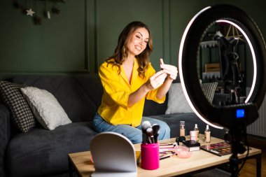 Güzellik vlogcusu evde makyaj dersi çekiyordu. Kanepede oturuyor ve rujdan bahsediyor..