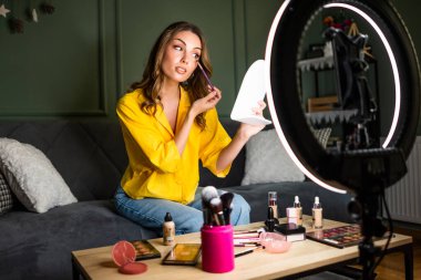 Güzellik vlogcusu evde makyaj dersi çekiyordu. Kanepede oturuyor ve halka ışığı ve akıllı telefonla video kaydediyor..