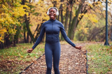 Kendinden geçmiş koşucu, düşen yaprakların peşinde koşar. Altın ve yeşil ağaçlar, dingin ve mevsimsel bir zemin oluşturur..