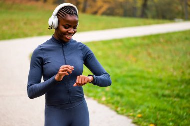 Karanlık atletizm kıyafetleri içinde bir koşucu güvenli bir şekilde ormanlık bir patikada koşar. Akıllı seke bakıyor..