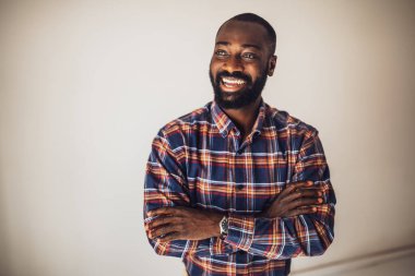 Kollarını kavuşturup gülümseyerek duvarda uzanan rahat gömlekli mutlu siyah adam..