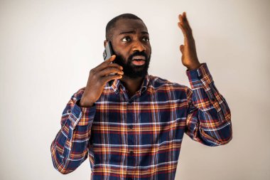 Rahat gömlekli endişeli siyah adam duvarın önünde duruyor ve cep telefonuyla konuşuyor..