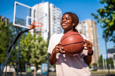 Afrika kökenli Amerikalı kadın oyuncu yaz antrenmanı sırasında top tutuyor ve gülüyor. Aktif yaşam tarzı ve şehir sporları.
