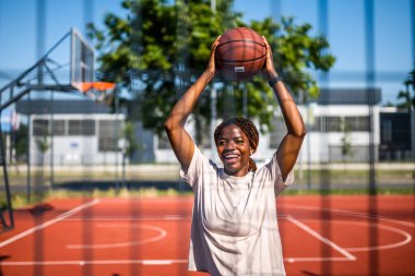 Afrika kökenli Amerikalı kadın oyuncu yaz antrenmanı sırasında top tutuyor ve gülüyor. Aktif yaşam tarzı ve şehir sporları.