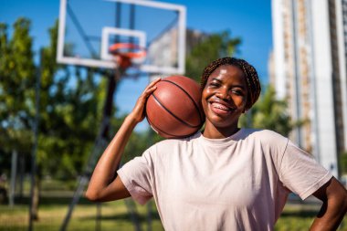 Açık şehir sahasında basketbol oynarken gülümseyen genç Afrikalı Amerikalı kadın..