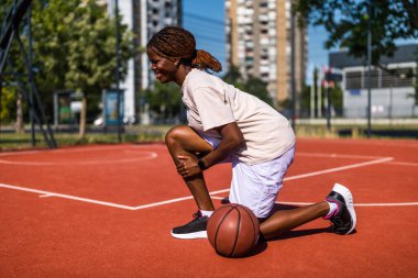 Genç bir kadın sabah spor salonunda tek başına basketbol oynuyor. Dizinde ağrı var..