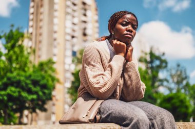Şehir parkında oturan, duygusal stresle uğraşan depresif Afrikalı Amerikalı bir kadının şehir tarzı portresi..