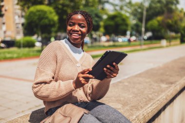 Çevrimiçi iletişim için dijital tablet kullanan neşeli bir zenci kadının portresi. İşten sonra dışarıda dinleniyor..