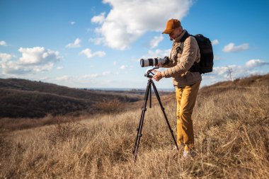 Vahşi yaşam kıdemli fotoğrafçısı tripodu kullanıyor ve güneşli bir günde açık bir kırsal alana büyük bir telefon lensi yerleştiriyor..