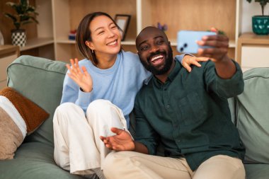 Neşeli, çok kültürlü bir çift yeşil bir kanepede yan yana oturur. Sıcak, modern bir oturma odasında gülüp kucaklaşırlar. Selfie çekiyorlar..