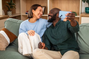 Neşeli, çok kültürlü bir çift yeşil bir kanepede yan yana oturur. Sıcak, modern bir oturma odasında gülüp kucaklaşırlar. Selfie çekiyorlar..