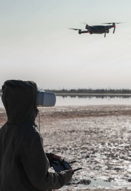 Turist yeni yerler keşfediyor. Kuadkopterle doğada İHA pilotu. Göl kenarında dururken insansız hava aracı kullanmak. İnsansız hava aracı ve sanal gerçeklik izleyicisi olan genç kişi.