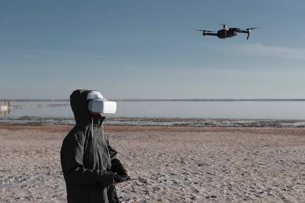 Turist yeni yerler keşfediyor. Kuadkopterle doğada İHA pilotu. Göl kenarında dururken insansız hava aracı kullanmak. İnsansız hava aracı ve sanal gerçeklik izleyicisi olan genç kişi.