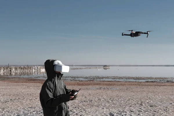 Turist yeni yerler keşfediyor. Kuadkopterle doğada İHA pilotu. Göl kenarında dururken insansız hava aracı kullanmak. İnsansız hava aracı ve sanal gerçeklik izleyicisi olan genç kişi.