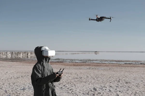 Turist yeni yerler keşfediyor. Kuadkopterle doğada İHA pilotu. Göl kenarında dururken insansız hava aracı kullanmak. İnsansız hava aracı ve sanal gerçeklik izleyicisi olan genç kişi.