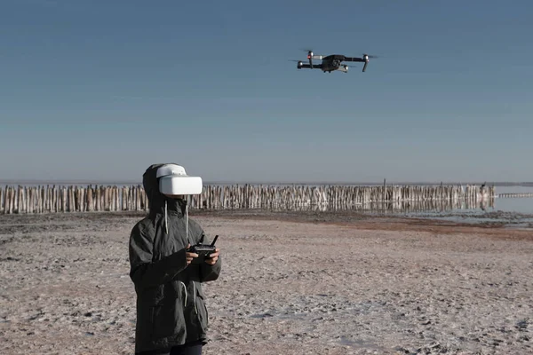 Turist yeni yerler keşfediyor. Kuadkopterle doğada İHA pilotu. Göl kenarında dururken insansız hava aracı kullanmak. İnsansız hava aracı ve sanal gerçeklik izleyicisi olan genç kişi.