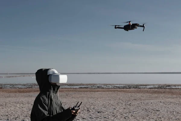 Turist yeni yerler keşfediyor. Kuadkopterle doğada İHA pilotu. Göl kenarında dururken insansız hava aracı kullanmak. İnsansız hava aracı ve sanal gerçeklik izleyicisi olan genç kişi.