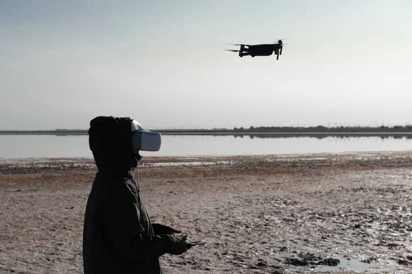 Turist yeni yerler keşfediyor. Kuadkopterle doğada İHA pilotu. Göl kenarında dururken insansız hava aracı kullanmak. İnsansız hava aracı ve sanal gerçeklik izleyicisi olan genç kişi.