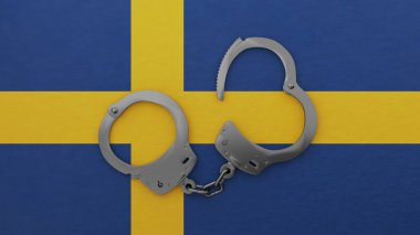 Yarı açık çelik kelepçe ortada ve İsveç bayrağının üstünde.