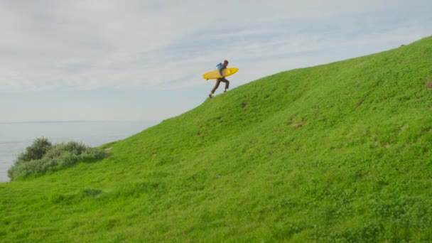 Um surfista carrega sua prancha para cima de uma colina — Vídeo de Stock
