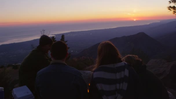 Amigos se sientan alrededor de una fogata en un campamento costero al atardecer — Vídeos de Stock