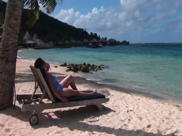 Μια γυναίκα που χαλαρώνει σε μια καρέκλα παραλία σε μια τροπική παραλία. — Αρχείο Βίντεο