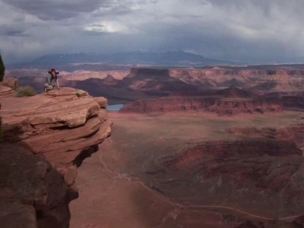 Un fotografo cammina verso una sporgenza che si affaccia su una valle di mesas — Video Stock