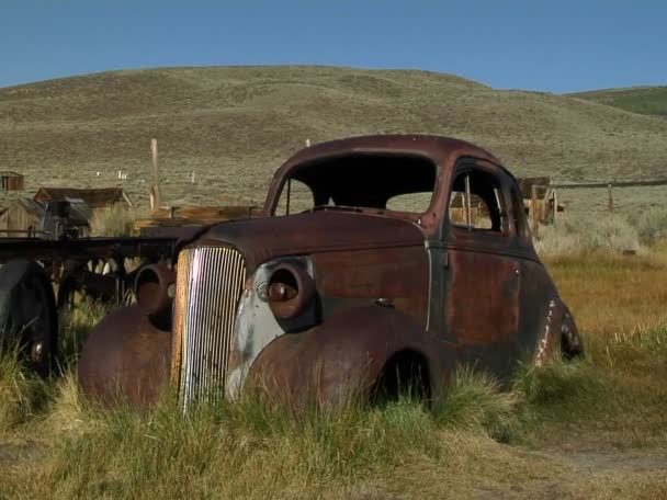 An old rusting car sits near an abandoned buildin — Stock Video