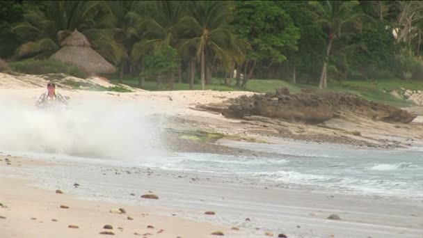 Un hombre monta un ATV a través del agua en la playa . — Vídeos de Stock