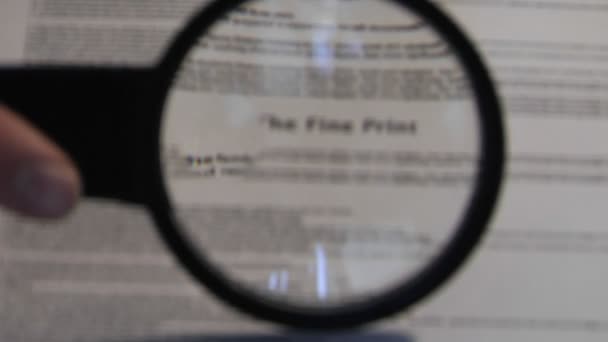 A magnifying glass passes over a paper revealing the words The Fine Print." — Stock Video