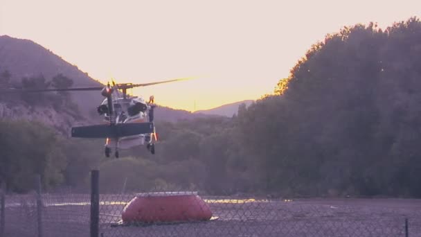 Požární helikoptéry čerpá vodu v horské zúčtování v rychlém pohybu. — Stock video