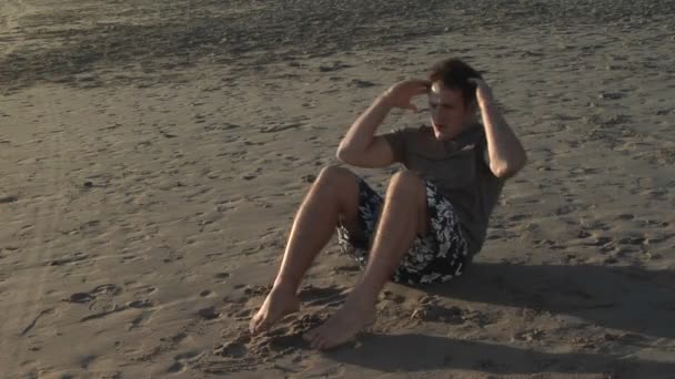 En man gör sit-ups på en sandstrand — Stockvideo