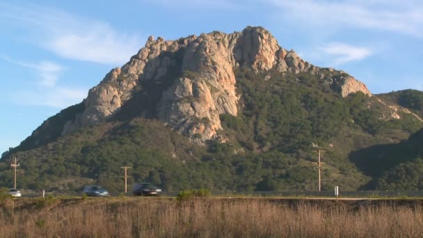 Una montaña se eleva a lo largo de una carretera ocupada — Vídeo de stock