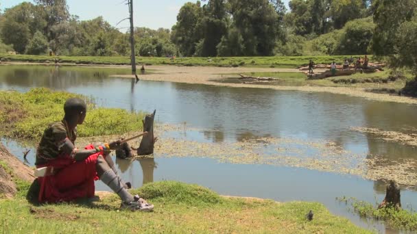 Masai menino senta-se ao lado do lago — Vídeo de Stock