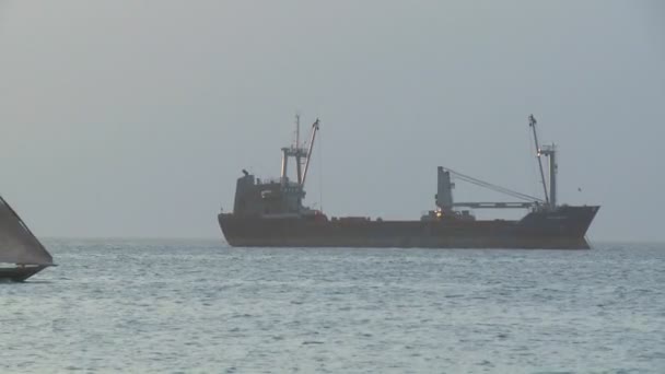 Een dhow zeilboot zeilen langs een vrachtschip — Stockvideo