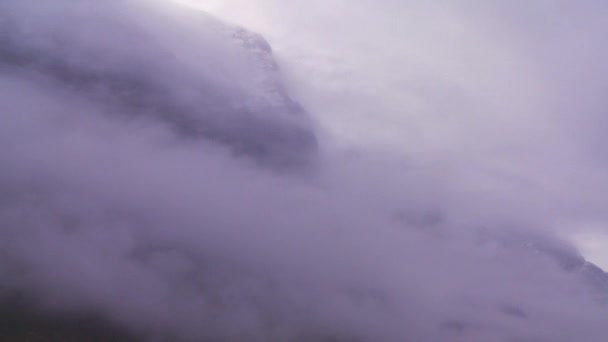 Nubes y niebla cuelgan revelan montañas a lo largo de un fiordo — Vídeo de stock