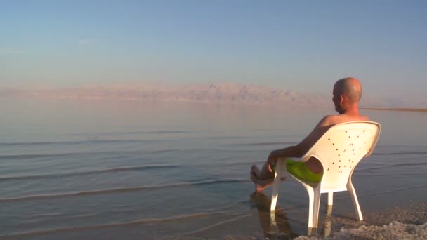 Hombre se sienta en la silla al lado del Mar Muerto — Vídeos de Stock