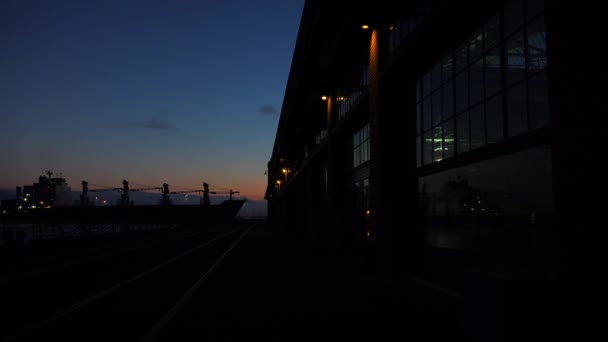 Cargo ship passes warehouse at dusk — Stock Video