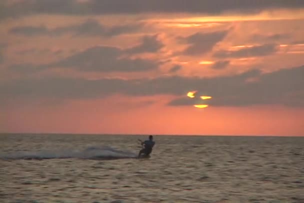 A windsurfer cuts across the water in silhouette against an orange sun. — Stock Video