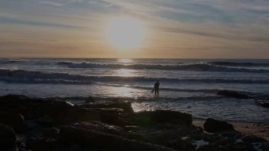 Gün batımında sudan çıkan sörfçü