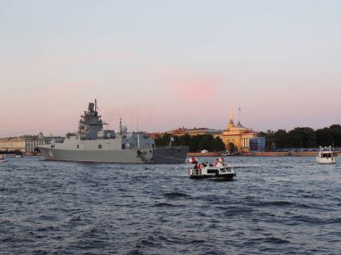 Gri bir savaş gemisi ve Neva Nehri 'ndeki birkaç motorlu tekne Winter Palace binasının arka planına karşı.      