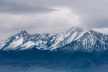 Bulutlu gri gökyüzü ile kayalık yüksek Tatras dağlarının karla kaplı tepeler