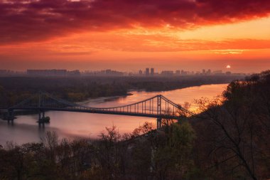 Gündoğumunda Dinyeper Nehri ve Volodymyrska Hirka parkından yaya köprüsü ya da Saint Volodymyr Tepesi manzaralı, Kiev (Kiev), Ukrayna. Ateşli gökyüzü ile güzel manzara